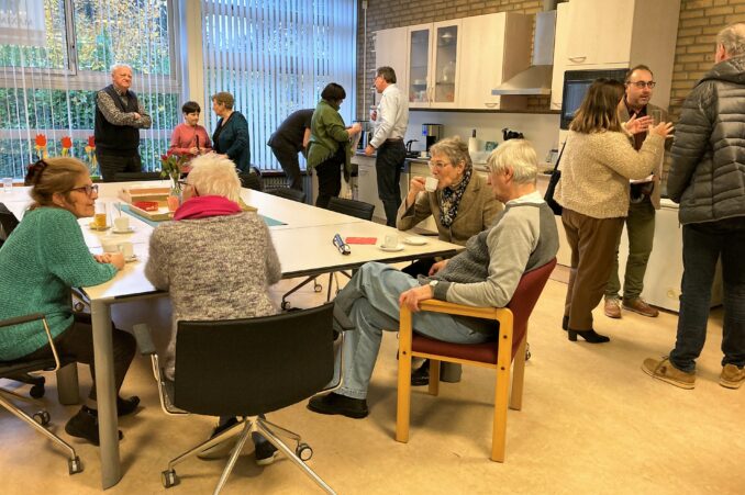 Gasten op de opening kletsen met elkaar en drinken koffie in de mooie keuken van de dagbesteding.