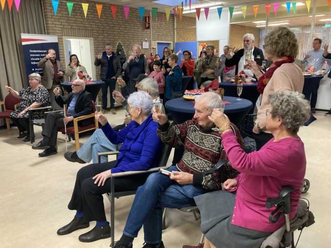 Alle aanwezigen proosten met een glaasje champagne op de opening van de dagbesteding.