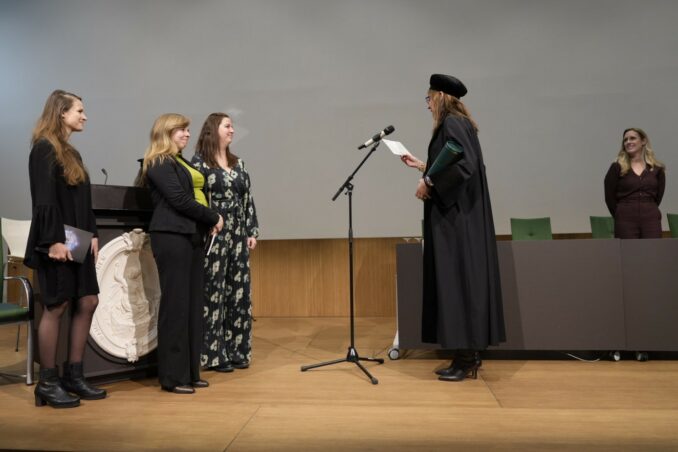Foto van promovendus Edine van Munster met aan haar zijden haar paranimfen, die toegesproken wordt door promotor Ruth van Nispen. Op de achtergrond copromotor Hilde van der Aa.